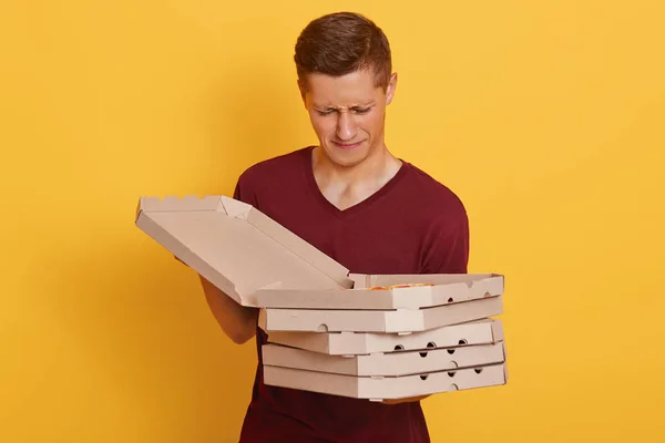 Imagen de un joven joven guapo decepcionado sosteniendo cajas de cartón, abriendo la caja con pizza, mirándola con disgusto, insatisfecho con la elección, entregando pizza equivocada. Concepto de personas y alimentos . — Foto de Stock