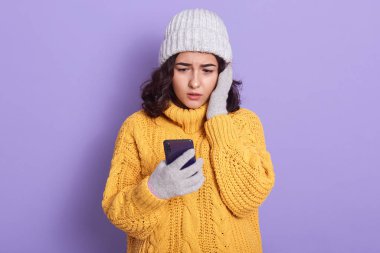 Image of shocked impressed reading news in net, looking at smartphone screen attentively with surprise, putting one hand on cheeck, having unpleasant facial expression. People and news concept.
