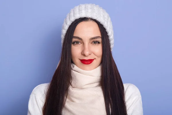 Image of magnetic attractive young black haired woman looking directly at camera, having red lips, wearing hat, sweater and scarf, having confident facial expression. People and emotions concept. — Stockfoto