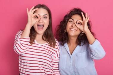 Güzel beyaz bir kadının portresini yakından çek. Parmaklarını gözünün önünde tutarken pembe arka planda duran, gündelik kıyafetler giyen, dışarıda eğlenen kadınlar gibi..