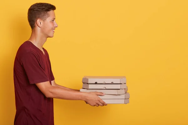 Boční pohled na doručovatele nosit kaštanové ležérní tričko dává jídlo objednávky pizza boxy izolované přes žluté pozadí studia. Koncepce služeb a dodávek. Kopírovat prostor pro reklamu nebo propagaci. — Stock fotografie