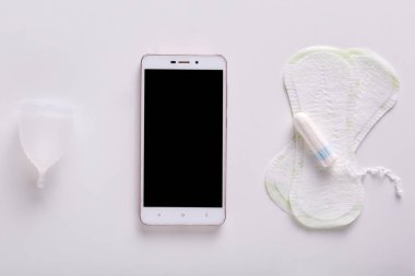Flat lay of smartphone with blank screen, tampon, hygiene menstrual pads laying over white background, menstrual cycle tracking, better option to use, collecting information. Menstrual periods concept clipart