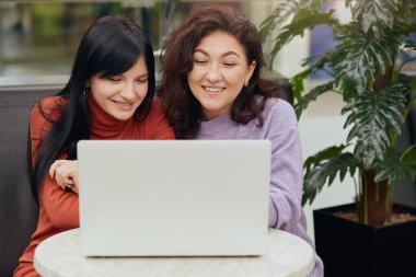 Neşeli manyetik pozitif esmerlerin yatay resmi laptopa dikkatle bakıyor, samimi bir şekilde gülümsüyor, kafede vakit geçiriyor, videolar izliyor, boş zamanların tadını çıkarıyor. Arkadaşlık kavramı.