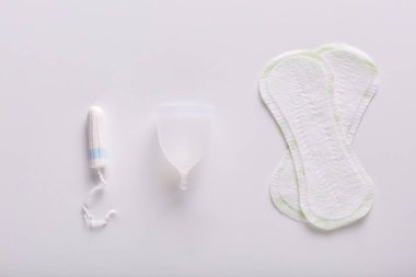Regl için çeşitli ürünlerin resmi. Hijyen pedleri, beyaz regl kupası ve beyaz yüzeyde duran tampon. Kritik günler için alternatif yollar. Kadınlar ve onların sorunları..