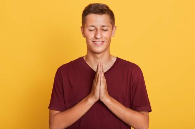 Enerjik, güzel saçlı, gözlerini kapayan, ellerini birleştiren, barışçıl bir jest yapan, meditasyon yapan, kırmızı tişört giyen genç bir çocuk görüntüsü. İnsanlar ve duygular.