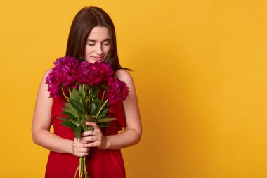 Elinde kestane rengi çiçeklerle çekici esmer bir kadının portresi, sarı arka planda saklanmış çiçekleri koklayan çekici bir kadın. Reklam veya tanıtım metni için boşluk kopyala.