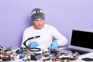 Elektronik cihazların hatalı yedek parçalarını tamir eden, teknoloji servisinde çalışan, gri şapkalı ve beyaz gömlekli genç bilgisayar rapair sihirbazının yatay görüntüsü..