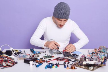 Elektronik cihazın hatalı yedek parçasıyla çalışan genç bir radyocunun görüntüsü. Gri şapkalı ve beyaz gömlekli yakışıklı bilgisayar rapair sihirbazı iş yerinde teknisyen.