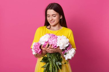 Yatay dişli, elinde çiçekle gülümseyen kadın, sarı elbiseli kadın, soyutlanmış pembe beyaz arka plan, erkek arkadaşından aldığı hediyeyle buketine bakan nazik kız..