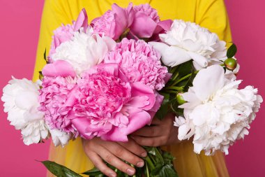 Sarı elbiseli, pembe ve beyaz şakayıklı çiçeklerden oluşan bir stüdyo resmi. Gül arkaplanda saklanmış şakayık çiçekleri olan yüzsüz bir kadın portresi. Kadınlar Günü konsepti