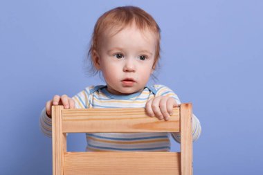 Yan yana bakan küçük bir çocuğun portresi. Stüdyoda mavi arka planda izole edilmiş bir sandalyede duruyor. Çizgili bir kazak giyiyor, dikkatli davranıyor, bir şeye odaklanıyor. Çocukluk kavramı.