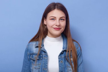 Beyaz kazak ve kot ceket giyen, uzun saçlı, doğrudan kameraya bakan, hoş bir yüz ifadesi olan çekici bir kadının yatay görüntüsü. Gençlik kavramı.