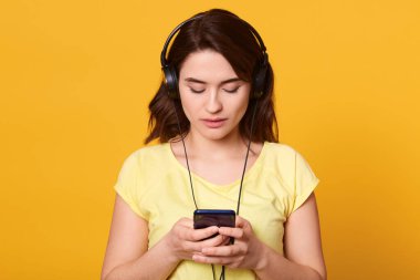 Esmer, ciddi bir kadının gündelik giysiler giydiği, akıllı telefonlardan müzik dinlediği stüdyoda arka planda izole edilmiş, cep telefonu tutan ve cihaza bakan bir görüntü..