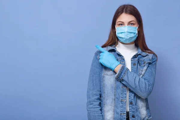 在蓝色背景下被隔离的女人的近照 女性穿着医用流感口罩和手套 把食指放在一边 公民19 广告复制空间 — 图库照片