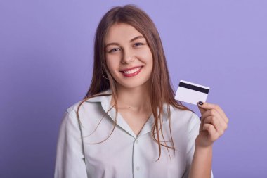 Genç ve güzel bir iş kadınının portresi elinde kredi kartıyla eflatun arkaplanından izole edilmiş poz veriyor doğrudan kameraya bakıyor internetten alışveriş yapan beyaz bluz giyen bir kadın..