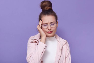 Baş ağrısı çeken, elini şakağa koyan, gözlerini kapalı tutan, leylak arkaplanının üzerinde tek başına duran, günlük kıyafetler giyen bir kız. Sorunlar, ateş, sağlık hizmeti kavramı.