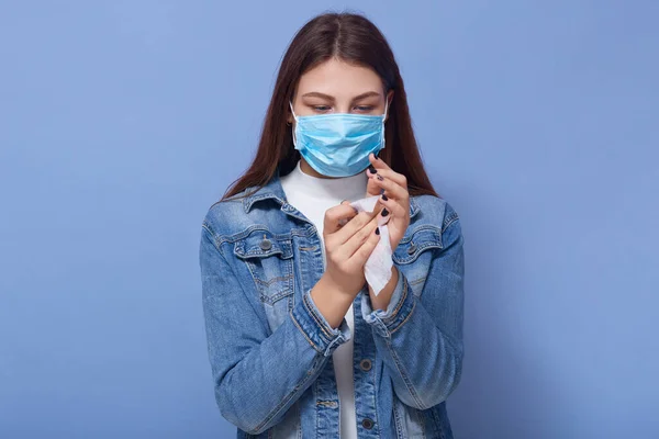 室内拍摄的妇女穿着时髦的防弹衣和医用蓝色面具 在工作室用蓝色背景擦拭双手 Coronavirus Covid Quarantine Health Care Concept — 图库照片