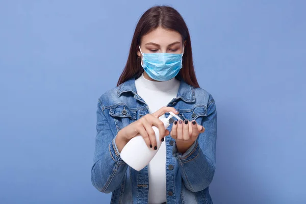 女性在流行期间使用液体肥皂喷雾的水平照 身穿白衬衫 牛仔夹克和蓝色一次性防护面罩的女士 Coranavirus Covid 检疫概念 — 图库照片