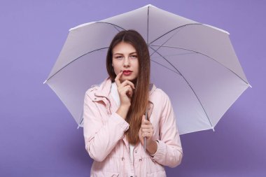 Düşünceli, özenli, çekici bir kadının şemsiyesini tutarken, bir parmağını Cheeck 'e koyarken, düşünceli bir yüz ifadesi takınırken, gündelik giysiler giyerken çekilmiş yatay bir fotoğraf. Hava tahmini kavramı.