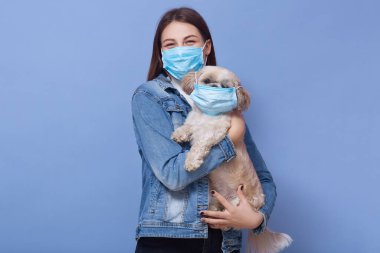 Kot ceket giyen, koruyucu flumaske takan, tıbbi maskeli köpek besleyen bir kadın. Coronavirus hastalığı insanlar ve evcil hayvanlar için tehlikelidir. Koronavirüs, salgın, qaurantine, önlem kavramı.