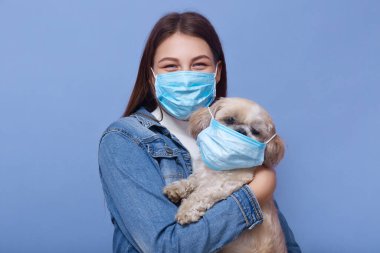 Virüsün yayılmasına karşı önlem olarak uzun saçlı, siyah ceketli ve tıbbi maskeli genç bir kadının portresi. Köpeğini de fluemaske ile elinde tutuyor. Coronavirüs salgını konsepti.