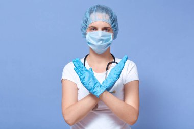 Tıbbi koruma maskesi takan bir kadın resmi, tıbbi şapka ve lastik eldiven, virüsü durdurmak için el ele tutuşan, epidemi, dünya pandemisi, mavi stüdyo arka planında izole edilmiş poz veren. Sağlık hizmeti kavramı