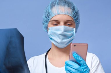 Kadın doktorun hastane ya da ofis kliniğinde telefonla konuşurken, omurilik taramalarını incelerken, Msk, şapka ve eldiven giyip bulgularını tartışmak için meslektaşını ararken yatay görüntüsü. Tedavi kavramı.