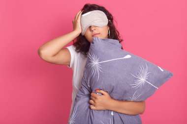 Pijama ve uyku maskesi takan, yastığı tutan, elini şakağa koyan, baş ağrısı çeken, rahat uyuyan genç bir bayanın yatay görüntüsü. İnsanlar ve uyku konsepti.