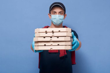 Closeup portrait of young guy handing pizza's boxes to customer, delivery man wearing protective mask and latex gloves, trying to avoid infection of coronavirus. Covid 19, quarantine concept. clipart