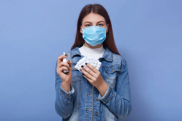 携带药丸和鼻腔喷雾剂的患病妇女的肖像 女性感染病毒 持有药物 需要特殊治疗 穿着斜纹棉布夹克 看着相机 隔离在蓝色的墙上 — 图库照片