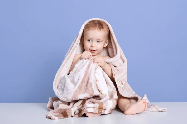 彼を洗浄した後 タオルに包まれたぬれた赤ちゃんの少年のイメージは 青いスタジオの壁に対して 脇を見て座って 赤ちゃんは入浴後にポーズをとって 毛布の下から足を見せて 子供は幸せそうに見えます — ストック写真