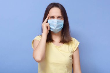 Kendine güvenen, antibakteriyel maske takan genç bir kadının yatay portresi. Mikrop kapmış, doğrudan kameraya bakıyor. Stüdyonun mavi arka planında tek başına duruyor. Covid19 konsepti.