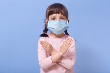 Stüdyo portresi, ellerini çarpıştıran, mesafesini koruyan, doğrudan kameraya bakan, evde kalan, diğerlerinden izole olan, tıbbi maske takan korkmuş küçük bir kızın portresi. Coronavirus konsepti.