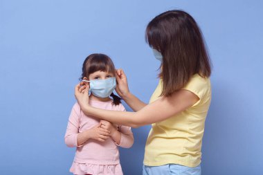 Şefkatli bir annenin, kızına antibakteriyel maske takması, karantina kurallarına uyması, evde kalması, karantinada kalması, stüdyoda mavi arka planda tek başına durması..