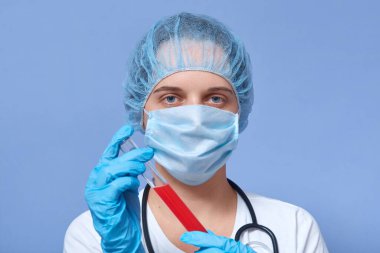 Tıbbi şapka, maske ve eldiven takan, 2019 için kan dolu test tüpü tutan, sonuçları bekleyen, tehlikeli bir iş yapan çok çalışan hemşire portresi. İnsanlar ve salgın konsepti.