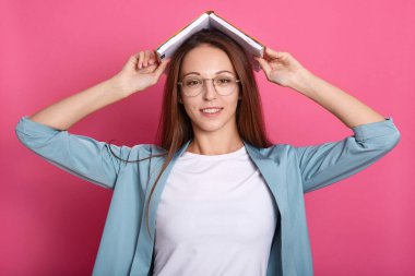 Manyetik güzel görünümlü genç bir bayanın portresi doğrudan kameraya bakıyor, açık kitabı kafaya koyuyor, oyuncu bir ruh hali içinde, yalnız başına rahatlıyor, içtenlikle gülümsüyor. Gençlik ve duygu kavramı.