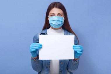 Elinde boş kağıtlar tutan, koruyucu maske ve eldiven takan, doğrudan kameraya bakan ve karantinada olan genç ve güzel bir kadının yatay portresi. Reklam için eşdeğer alan.