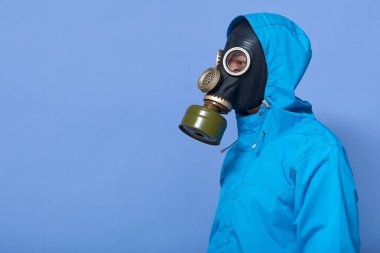 Korunma giysisi giyen, gaz maskeli, yalnız başına, zor durumda olan, mavi arka planda tek başına duran cesur bir adamın profili. Reklam için eşdeğer alan.