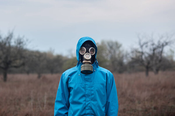Outside picture of stalker wearing blue jacket and gas mask, spending time alone, being at 30 km exclusion zone, doing illegal things, looking directly at camera. People and adrenaline concept.