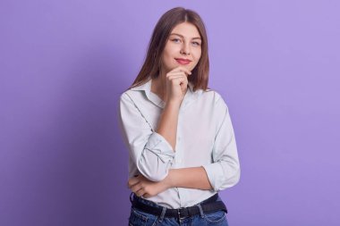 Çekici, düşünceli bir iş kadınının bir elini çenesine koyduğu, huzurlu bir yüz ifadesi takındığı, şık kıyafetler giydiği, hoş bir gülümsemeye sahip olduğu kapalı mekânlarda çekilmiş bir fotoğraf. İnsanlar ve iş kavramı.