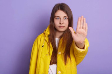 Ciddi bir kadının avuç içi hareketleriyle, sarı ceketi ve beyaz gömleğiyle, eflatun stüdyosunun arka planında izole bir şekilde poz verirken, uzun saçlı, çekici bir kadının görüntüsü. Halk konsepti.