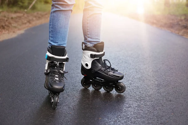 未知の人ローラースケートの水平方向の画像 ローラースケートはぬれた道路上にある 背景に太陽を持っている 日常生活の中で使用される黒の近代的なローラースケート レジャー活動 動きの概念 — ストック写真