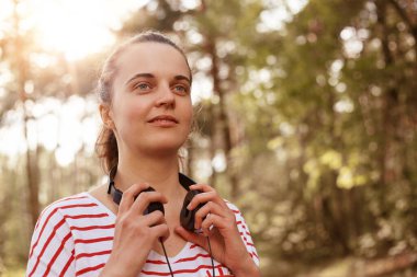 Yatay olarak güzel görünümlü çekici bir bayanın yürüdüğü, doğayla iç içe olduğu kulaklıklar taktığı, temiz hava soluduğu, çizgili kazak giydiği bir sahne. Doğa konsepti.