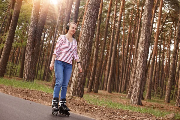 긍정적 다리에 로울러 스케이트 음악을 헤드폰 줄무늬 스웨터 매력적 여인의 — 스톡 사진