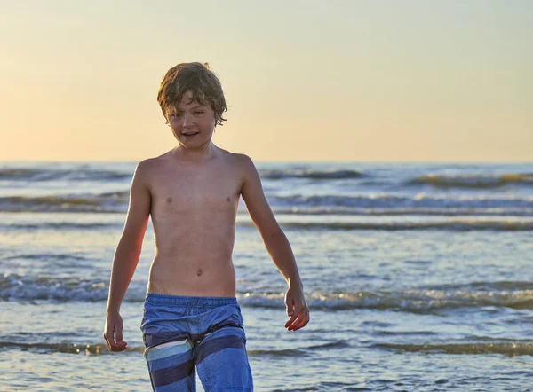 Günbatımı dalgalar halinde duran genç çocuk