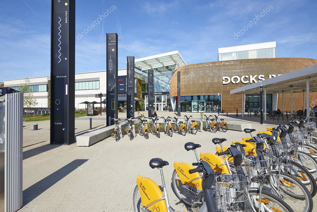 BRUSSELS, BELGIUM, 19 APRIL 2018: Stock of rental bike and some people resting at the Docks Bruxsel Main Entrance - New shopping district, in an area in full economic redeployment, a new quarter is hatching at schaerbeek, Brussels,Belgium