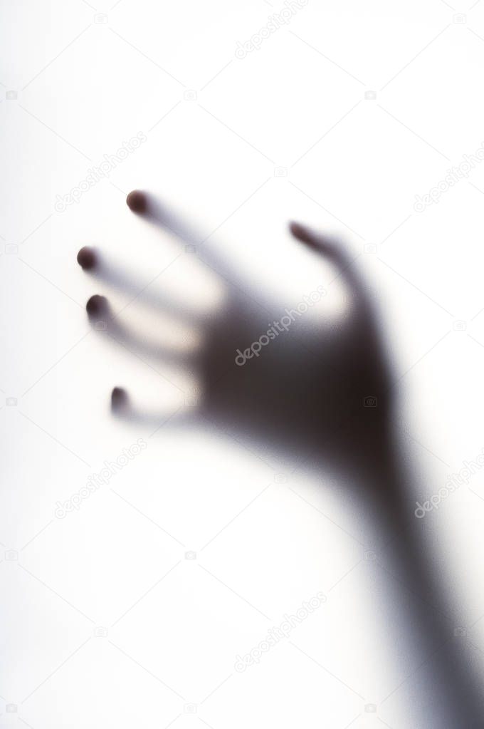 Diffused shadow of hand with thin fingers behind the frosted glass