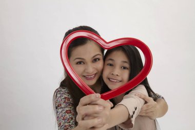 Malay anne ve kızı kamera karşı karşıya bir kırmızı kalp şekli resim çerçevesi holding