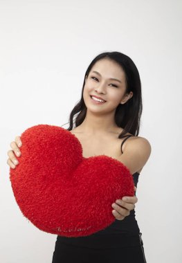 Asyalı kadın kırmızı kalp şeklinde yastık holding.