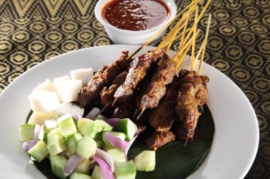 Malaysian food satay with the cucumber and keupat on the kain songket clipart